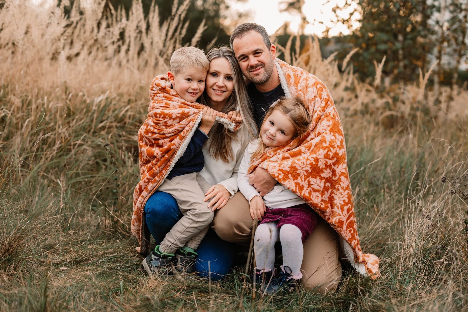 Three children sitting together on blanket in autumn field.