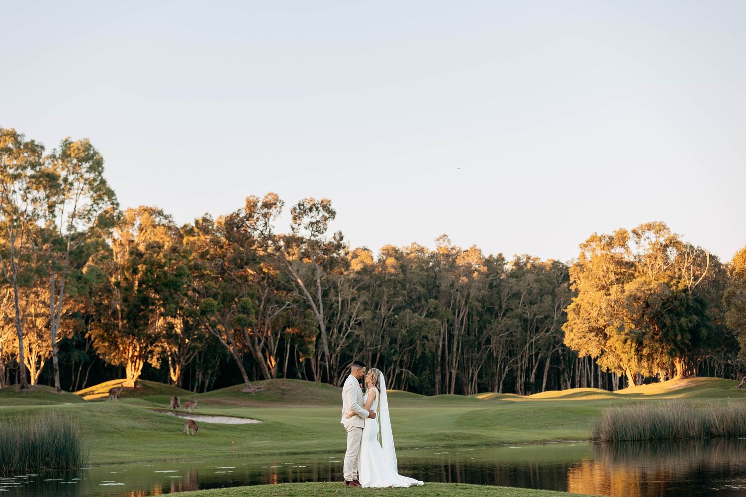 A couple walks hand in hand on a lush golf course at sunset with golden light illuminating the trees.