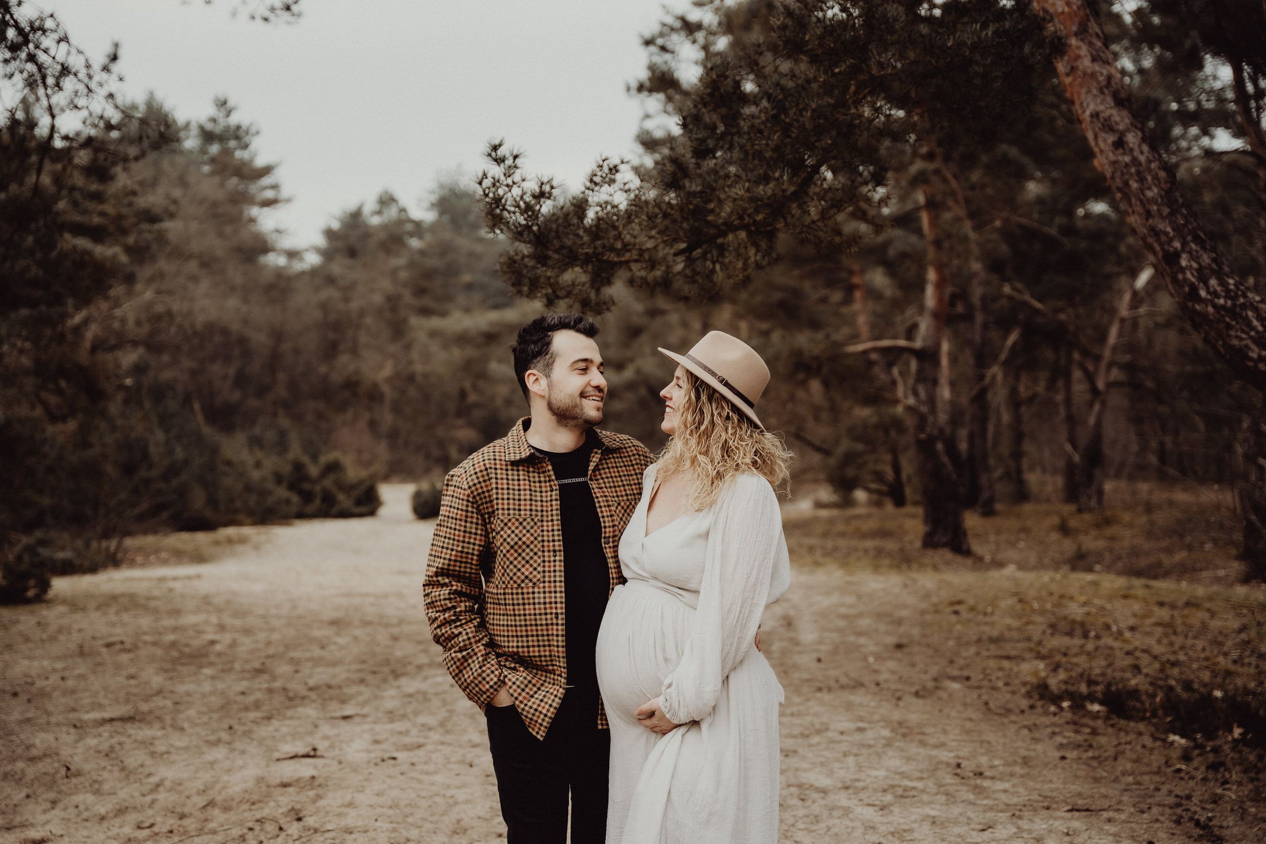 A couple stands on a forest path with one wearing a brown jacket and the other in white.