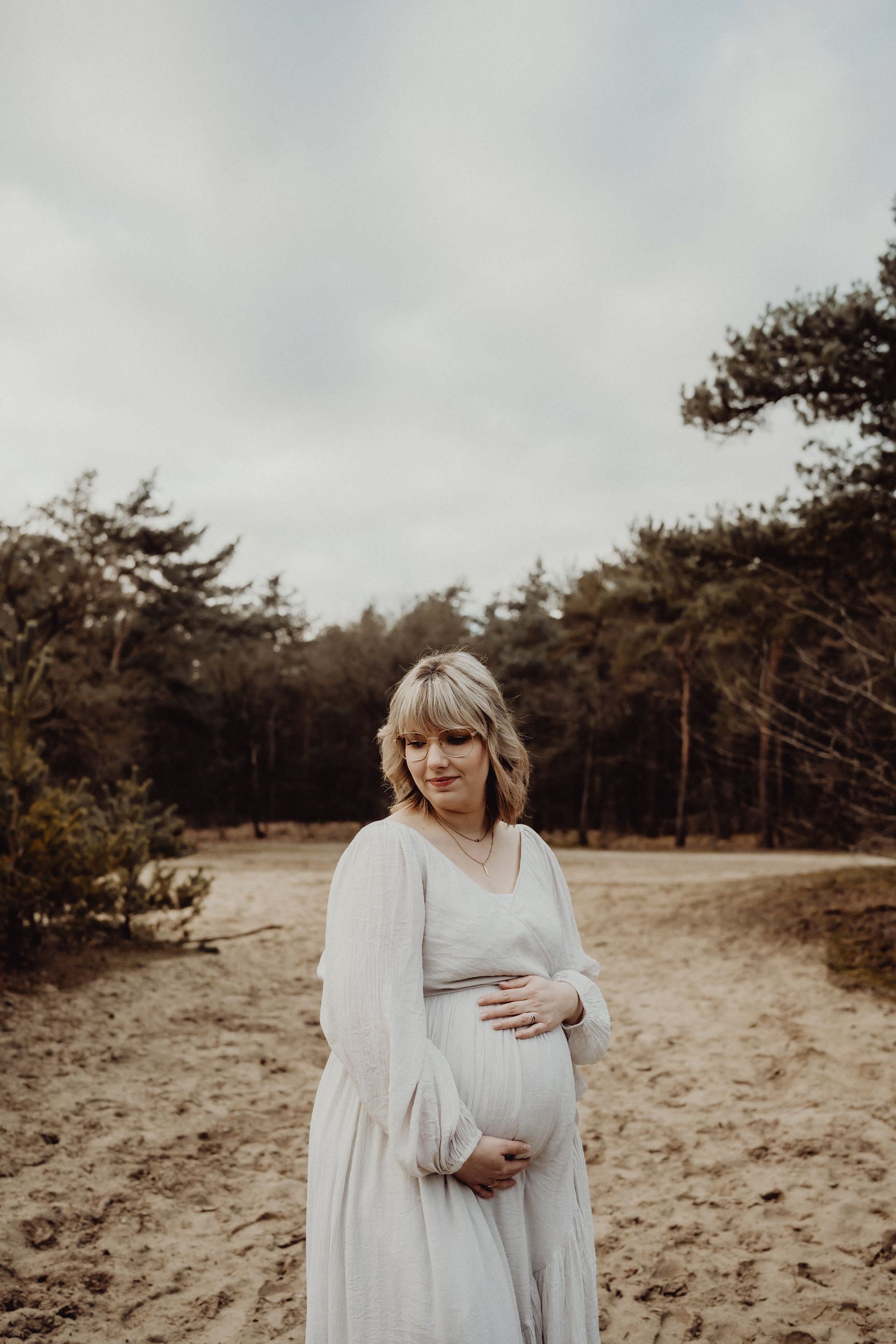 A white flowy dress glows in soft light against a pine forest backdrop.