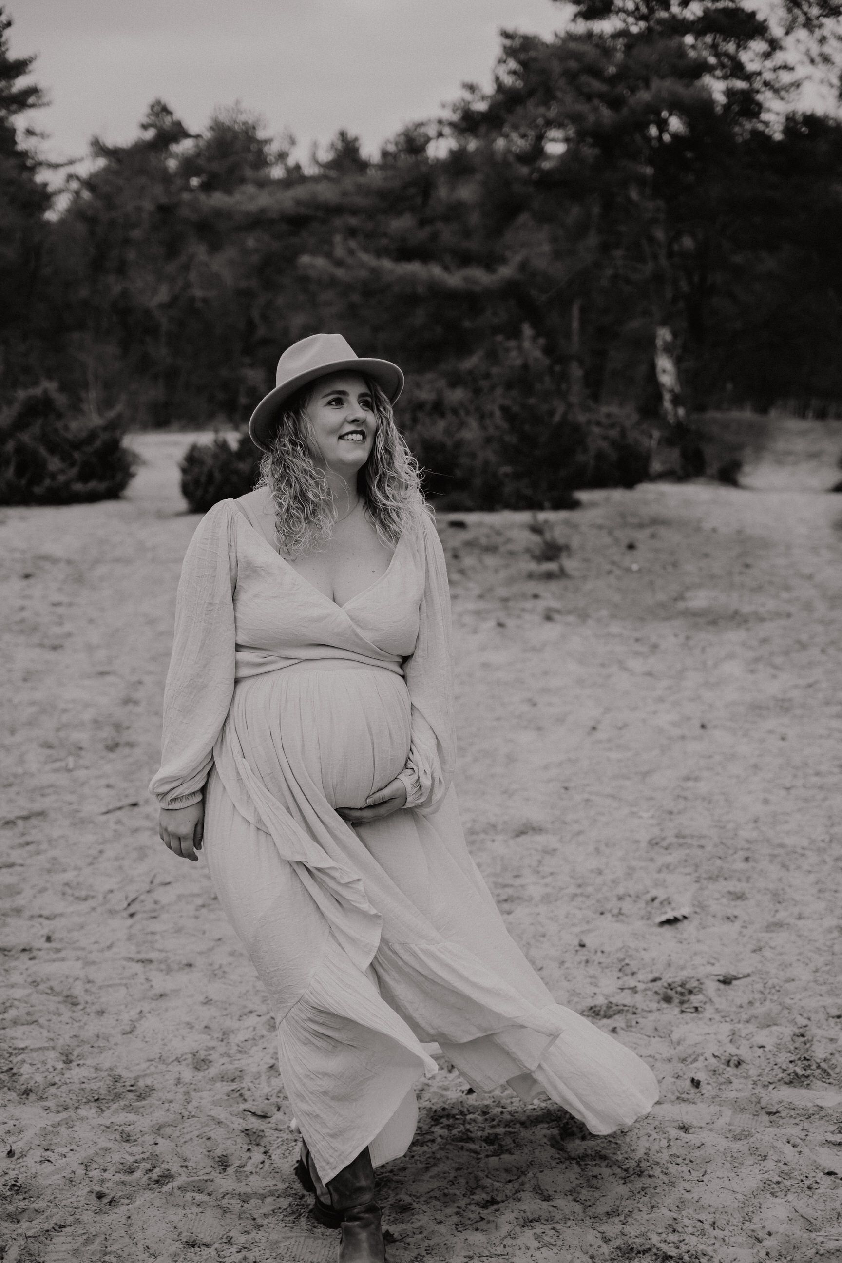 A maternity photoshoot in a natural outdoor setting with flowing dress and sun hat.