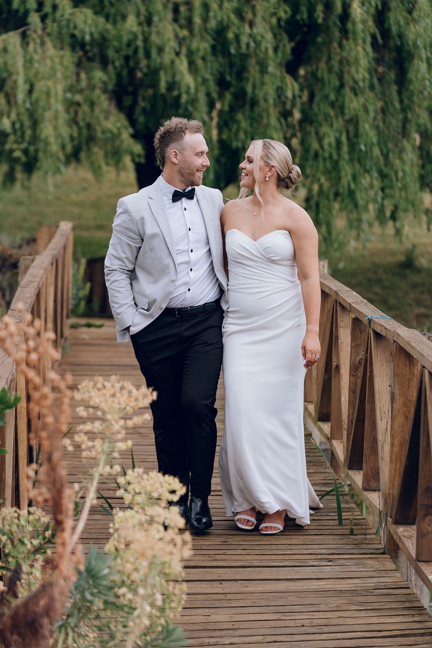 Couple in wedding attire sharing intimate moment on wooden bridge surrounded by nature.