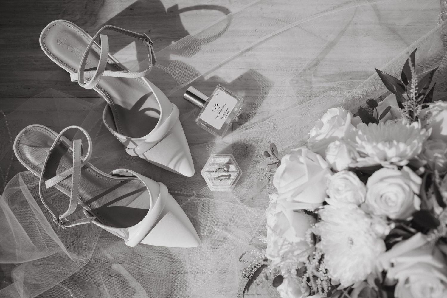 Wedding details flatlay with bridal shoes and white roses bouquet in black and white.