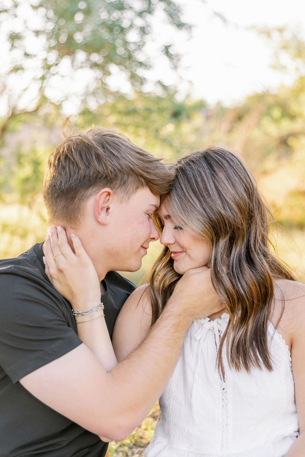 Romantic couple sharing an intimate moment in a sunlit outdoor setting with soft bokeh background.