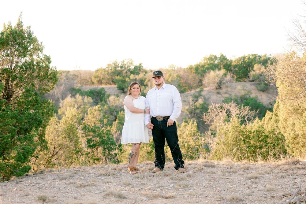 A couple poses together on a scenic hilltop during a sunset photoshoot surrounded by natural foliage.