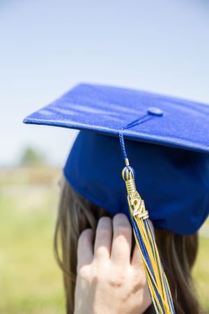 Cora Emilie Media Close-up of blue graduation cap with gold and blue tassel against sky background.