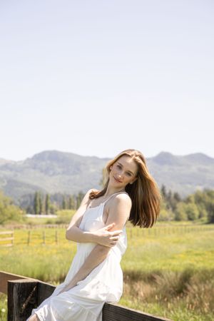 Cora Emilie Media Graduate poses in white dress against mountain backdrop during golden hour.
