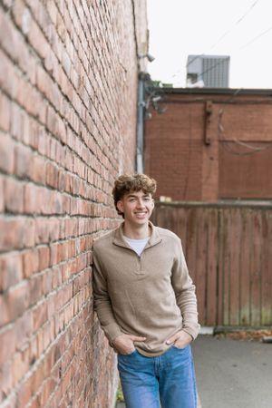 Cora Emilie Media Person in casual attire leaning against brick wall with relaxed pose.