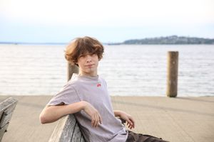 Cora Emilie Media Casual portrait of person on waterfront dock with cloudy sky and water behind.