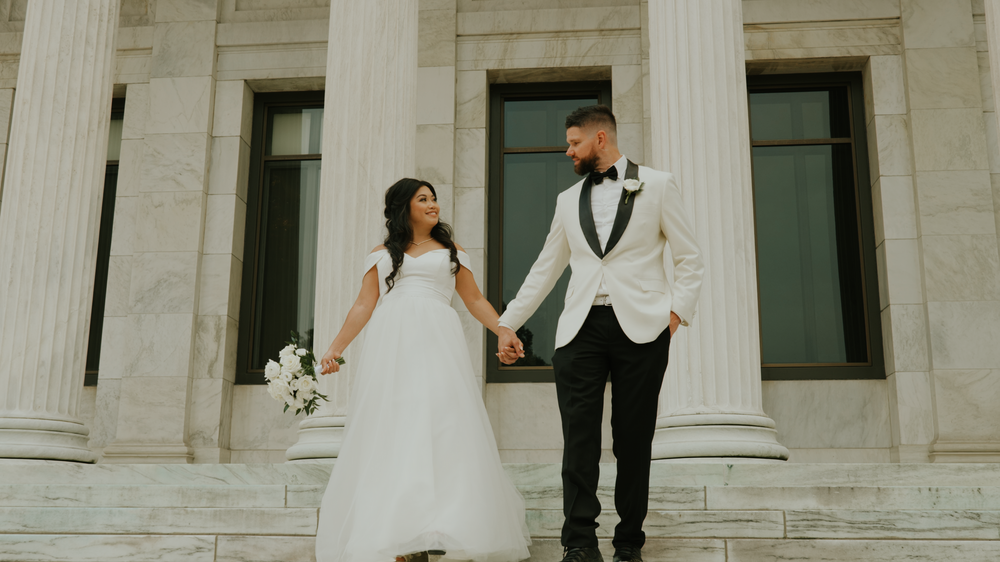 Bride and groom pose on classic white stone steps of historic building.
