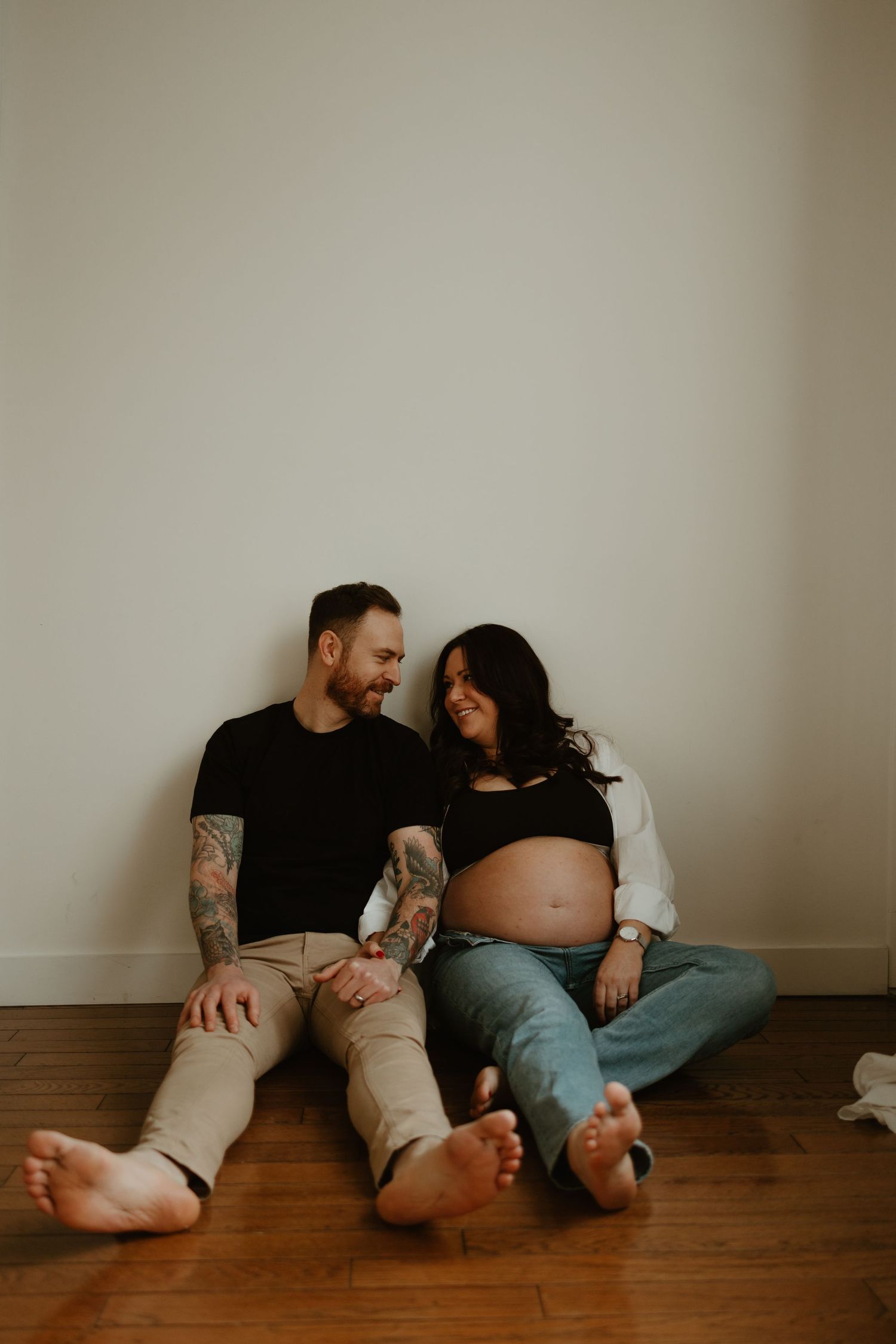 Minimalist maternity photos of couple relaxing on wooden floor.