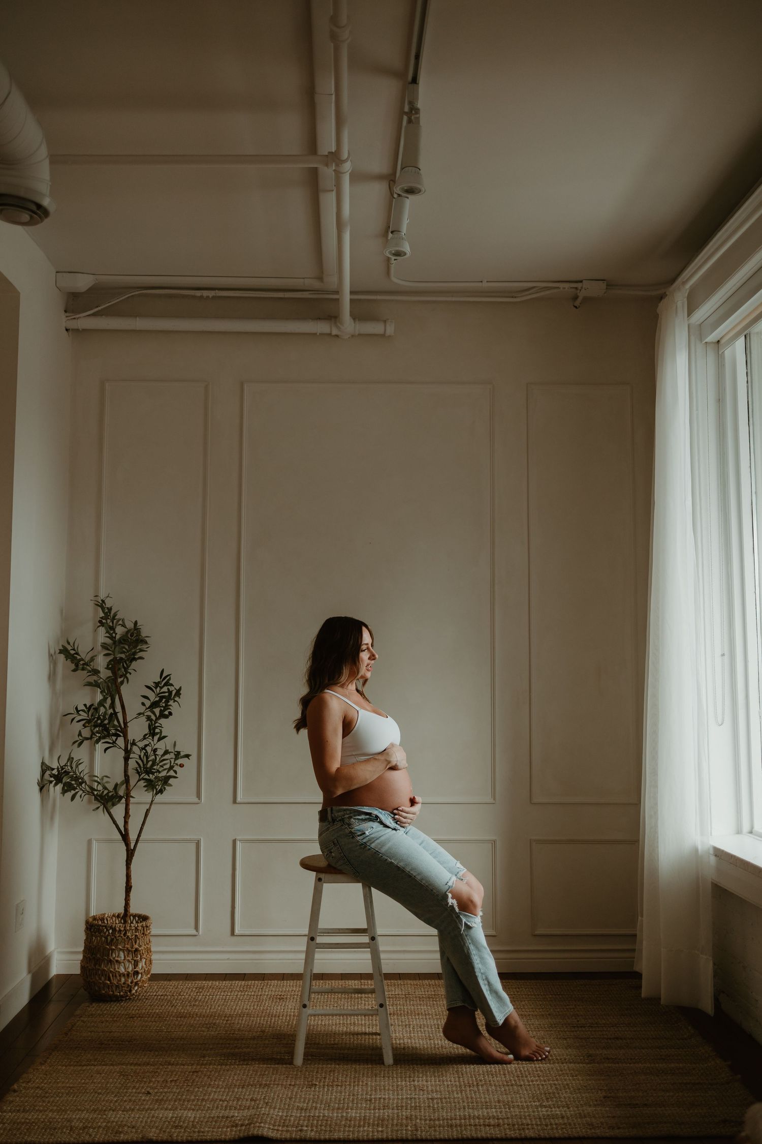 Artistic maternity portraits in minimalist white studio with window light.