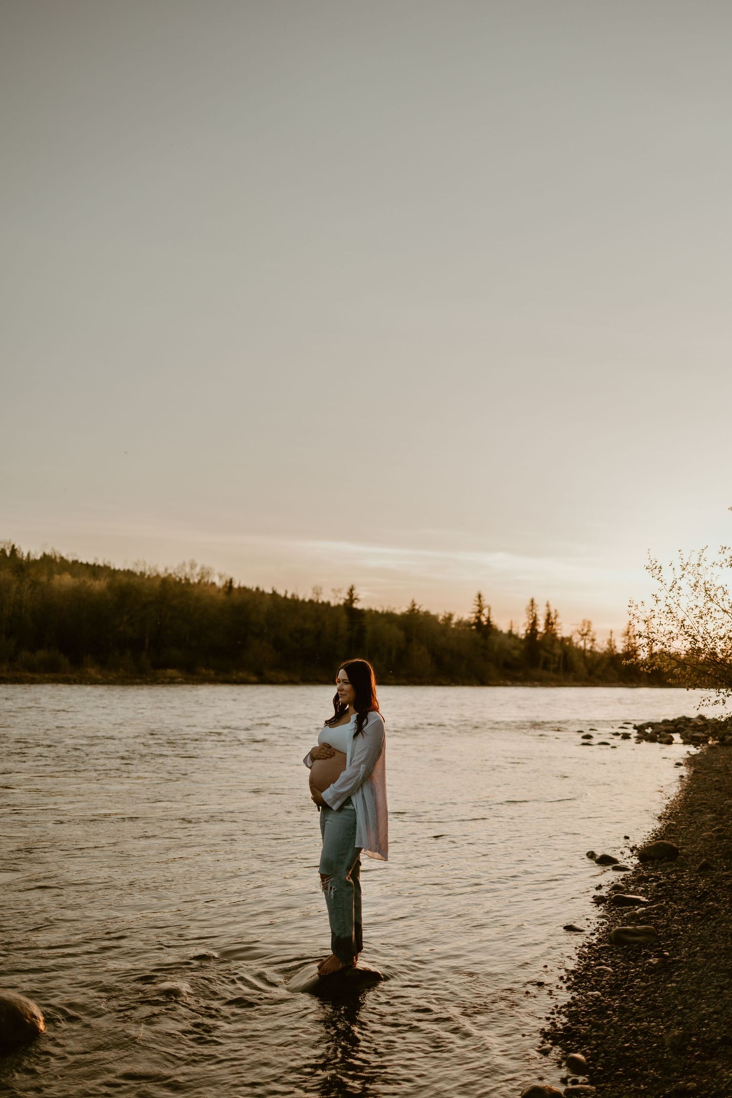People wading in lake water during sunset with forest backdrop.