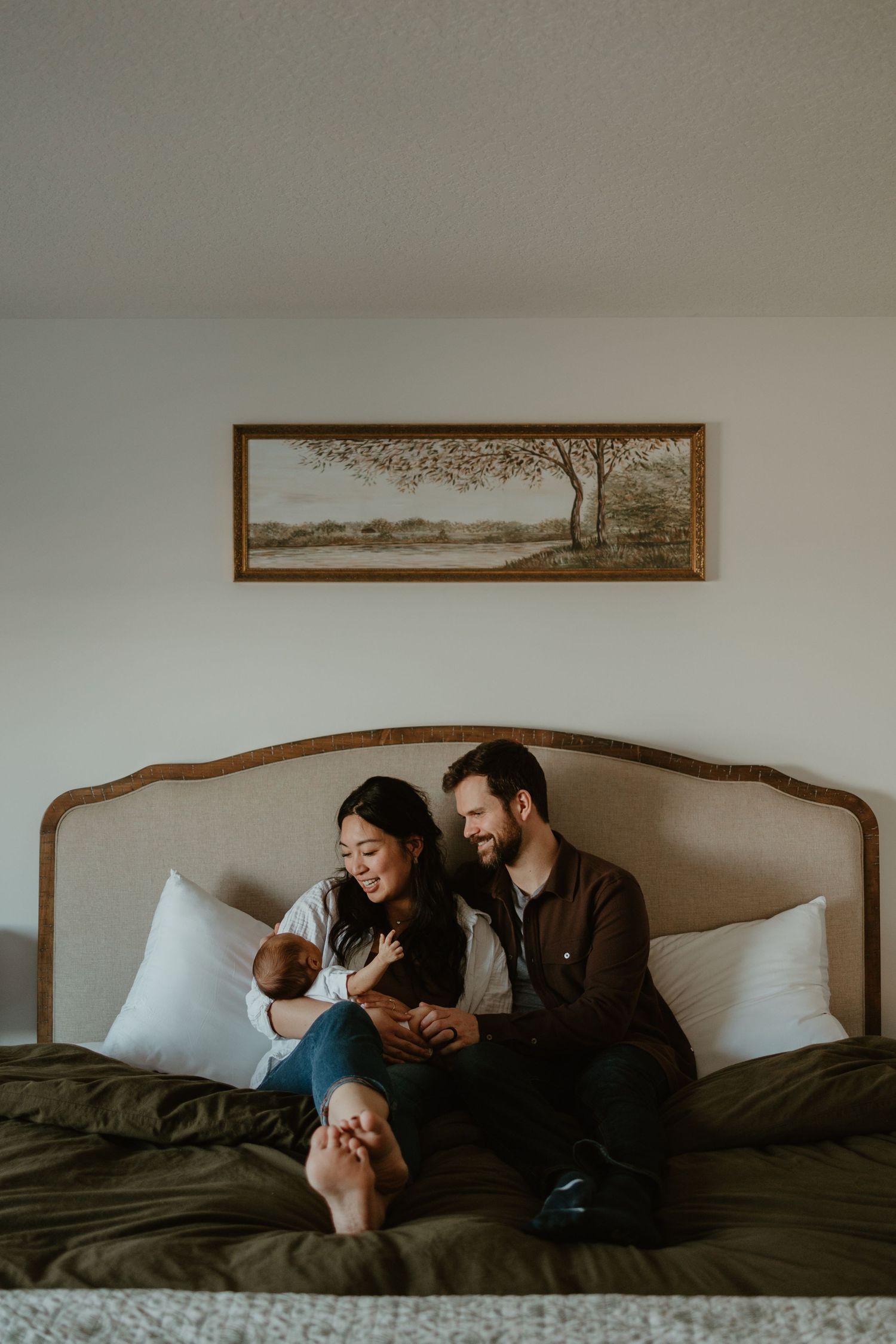 A cozy bedroom scene with a couple and baby relaxing together on a bed with decorative wall art.