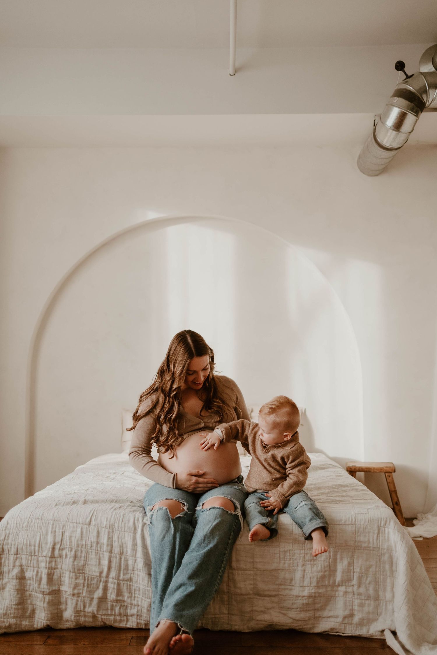 Tender moments between mother and baby on white bedding in natural light.