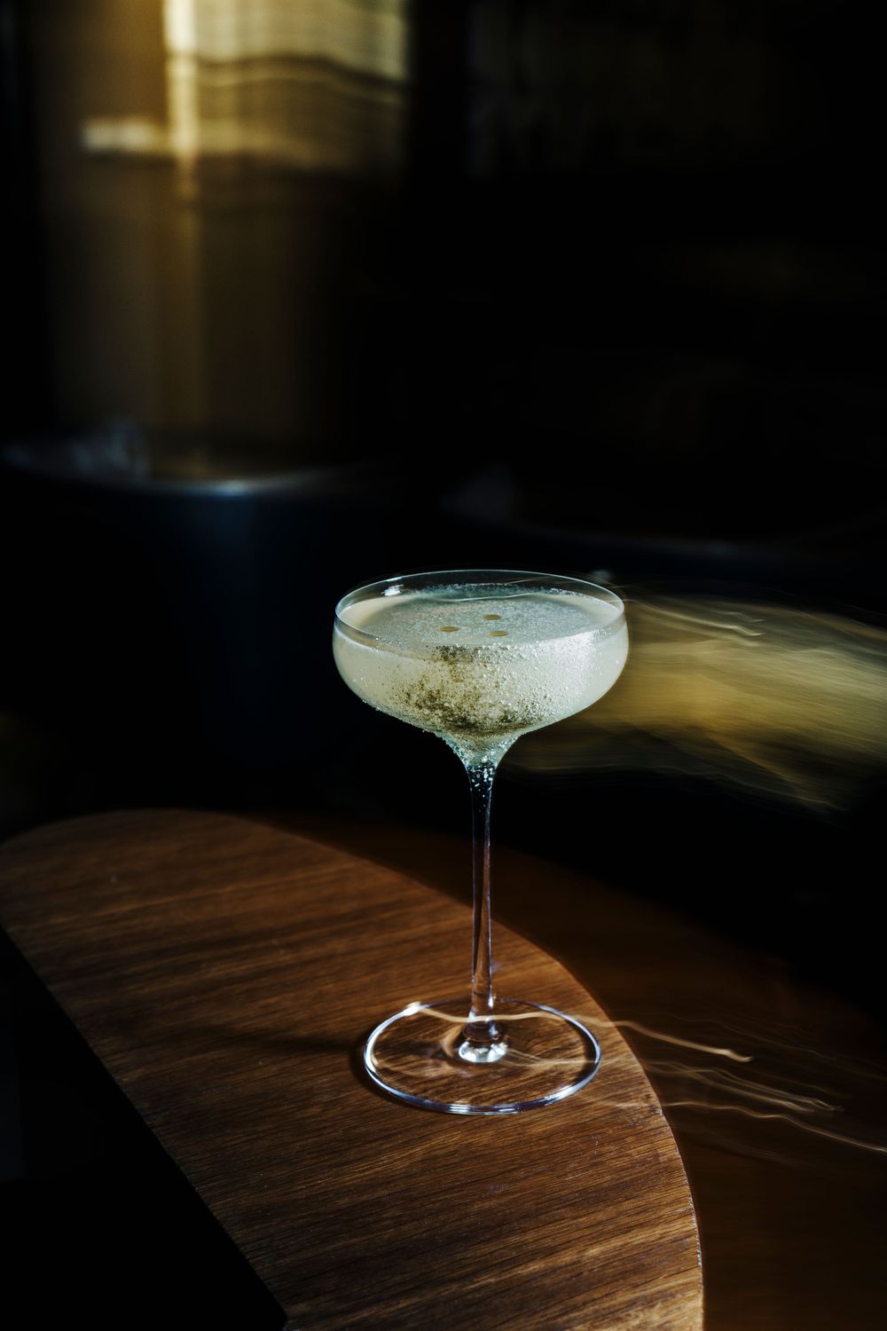Elegant cocktail glass with smoky garnish on wooden surface in dramatic lighting.
