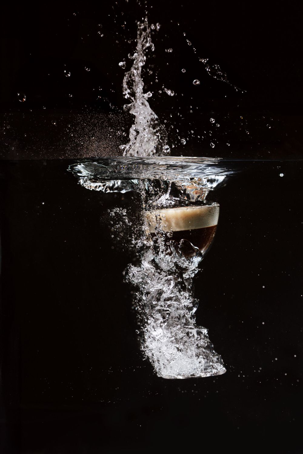 Dramatic splash photography of liquid falling into a cocktail glass against black background.