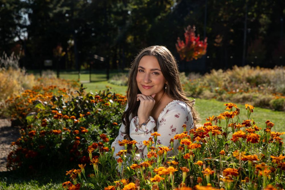 Young woman posing among vibrant orange flowers in a sunlit garden during autumn.