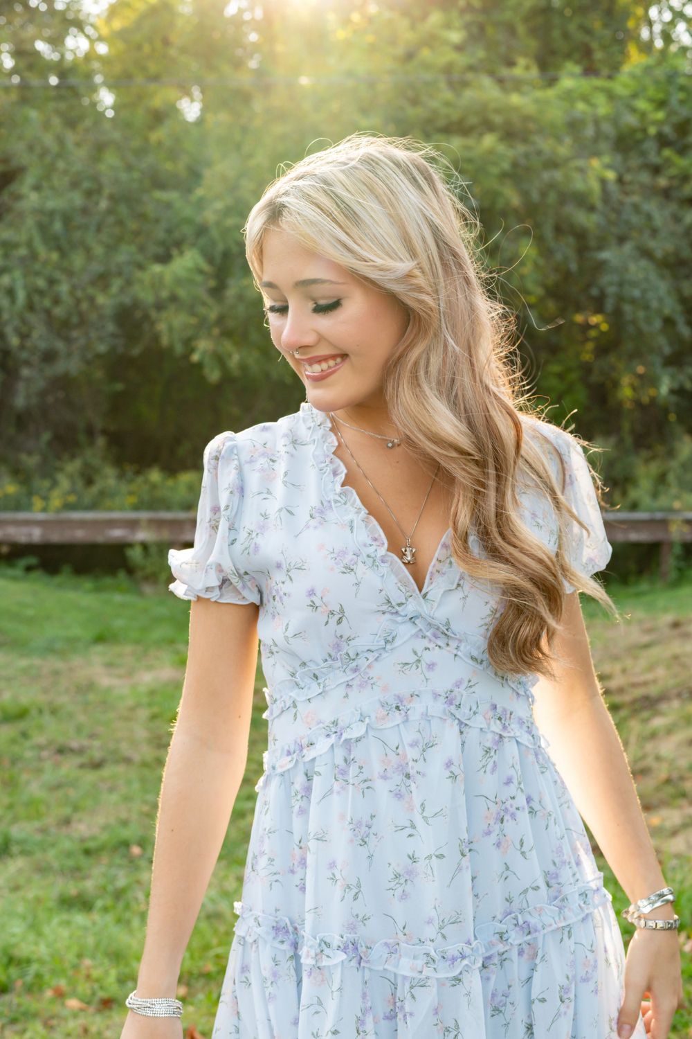 Blonde woman in light blue floral dress smiling outdoors in golden sunlight.