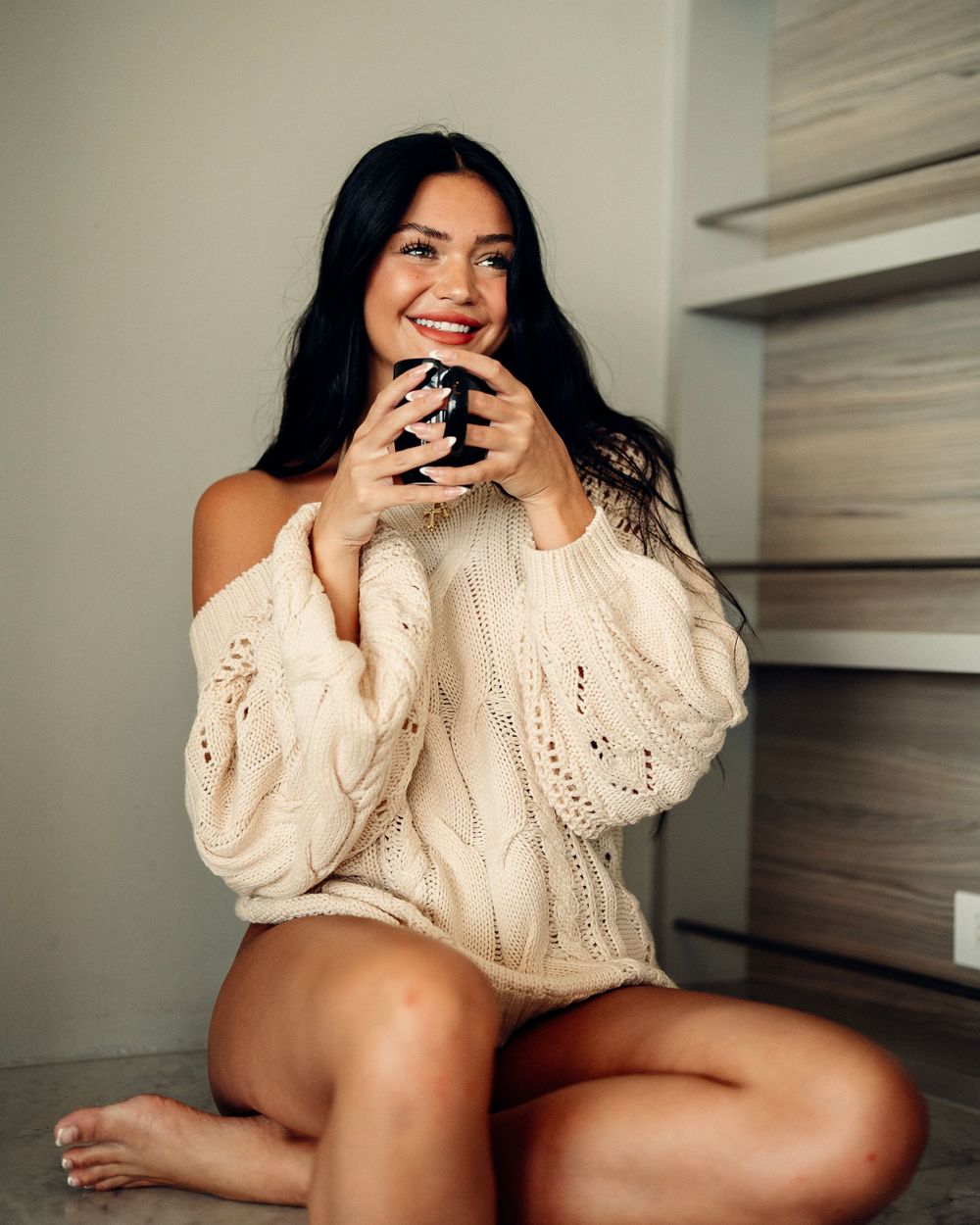 Person wearing white knit sweater poses on floor in natural indoor lighting creating intimate mood.