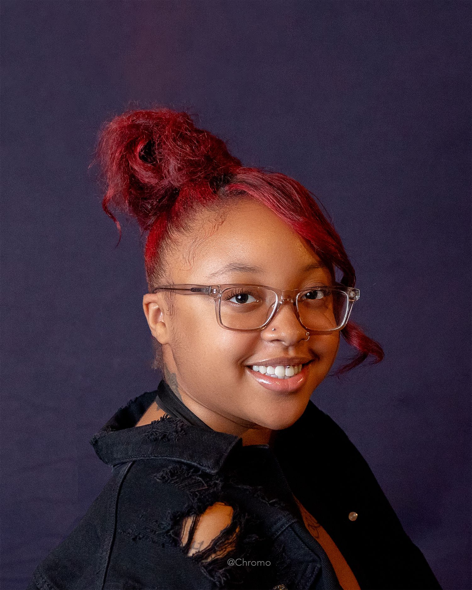 Portrait of a person with vibrant red hair styled in a bun wearing glasses and a black top.