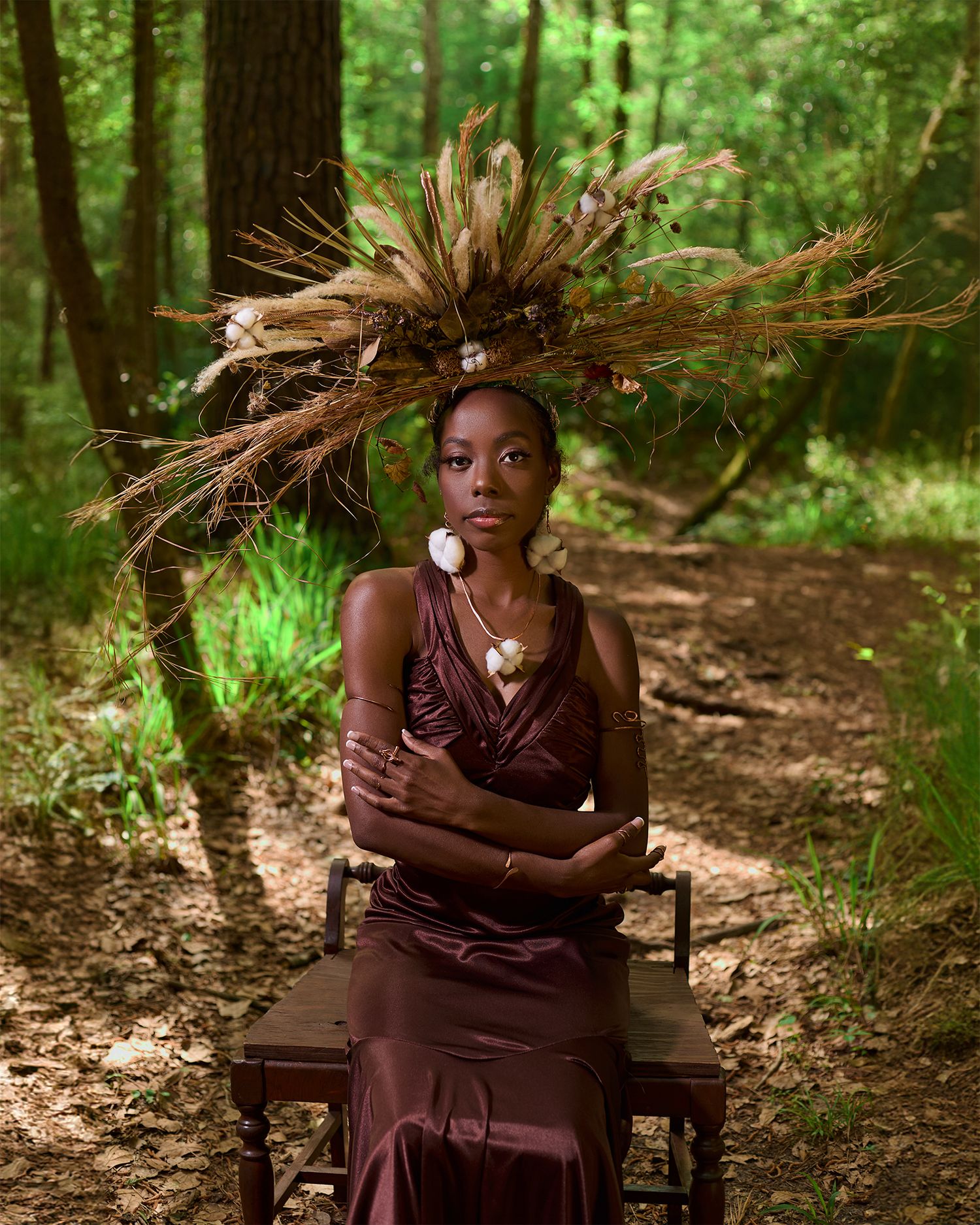 A artistic portrait in a forest setting with natural headdress and burgundy gown.