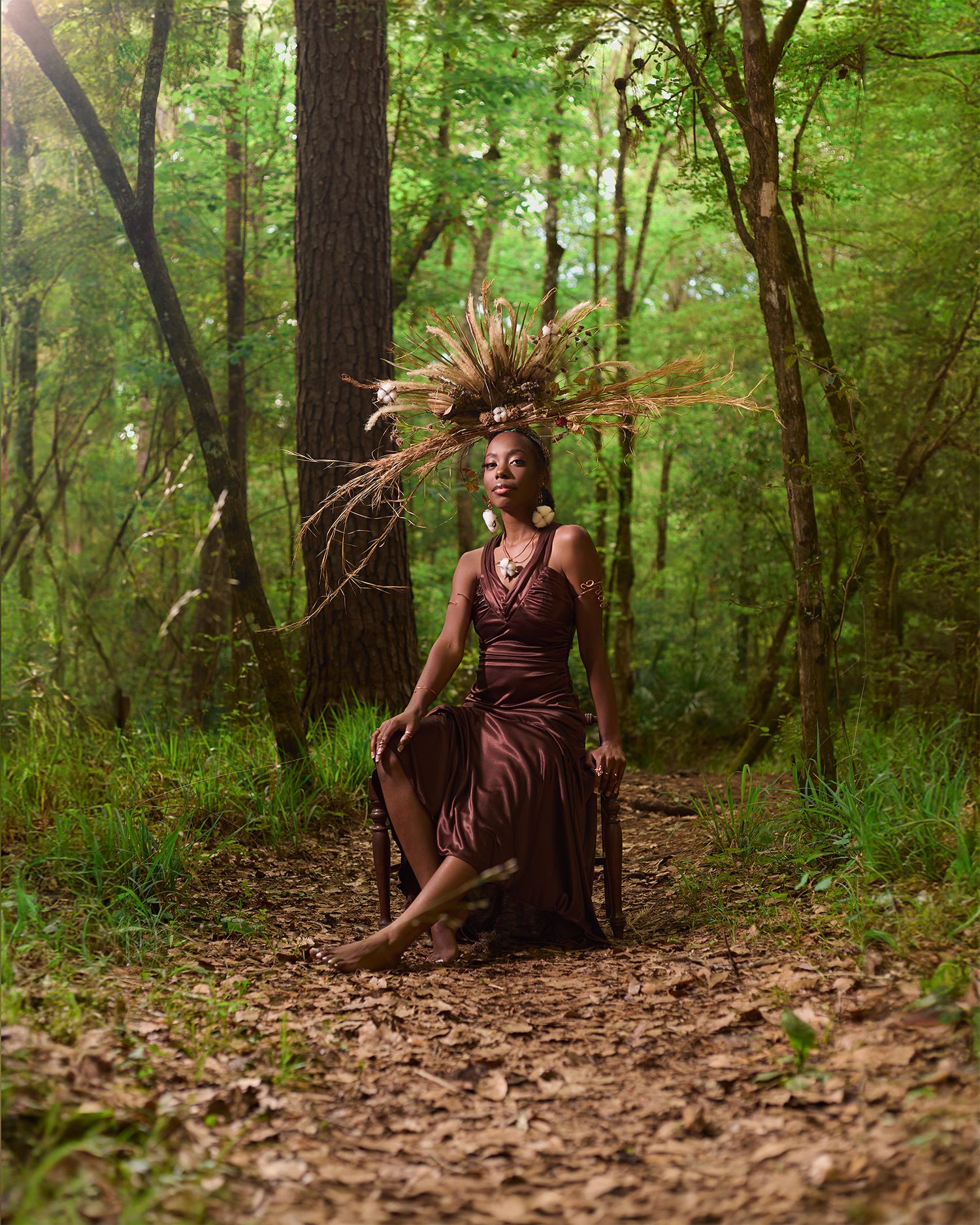 A forest fashion shoot features a dramatic dried grass crown and flowing burgundy dress.