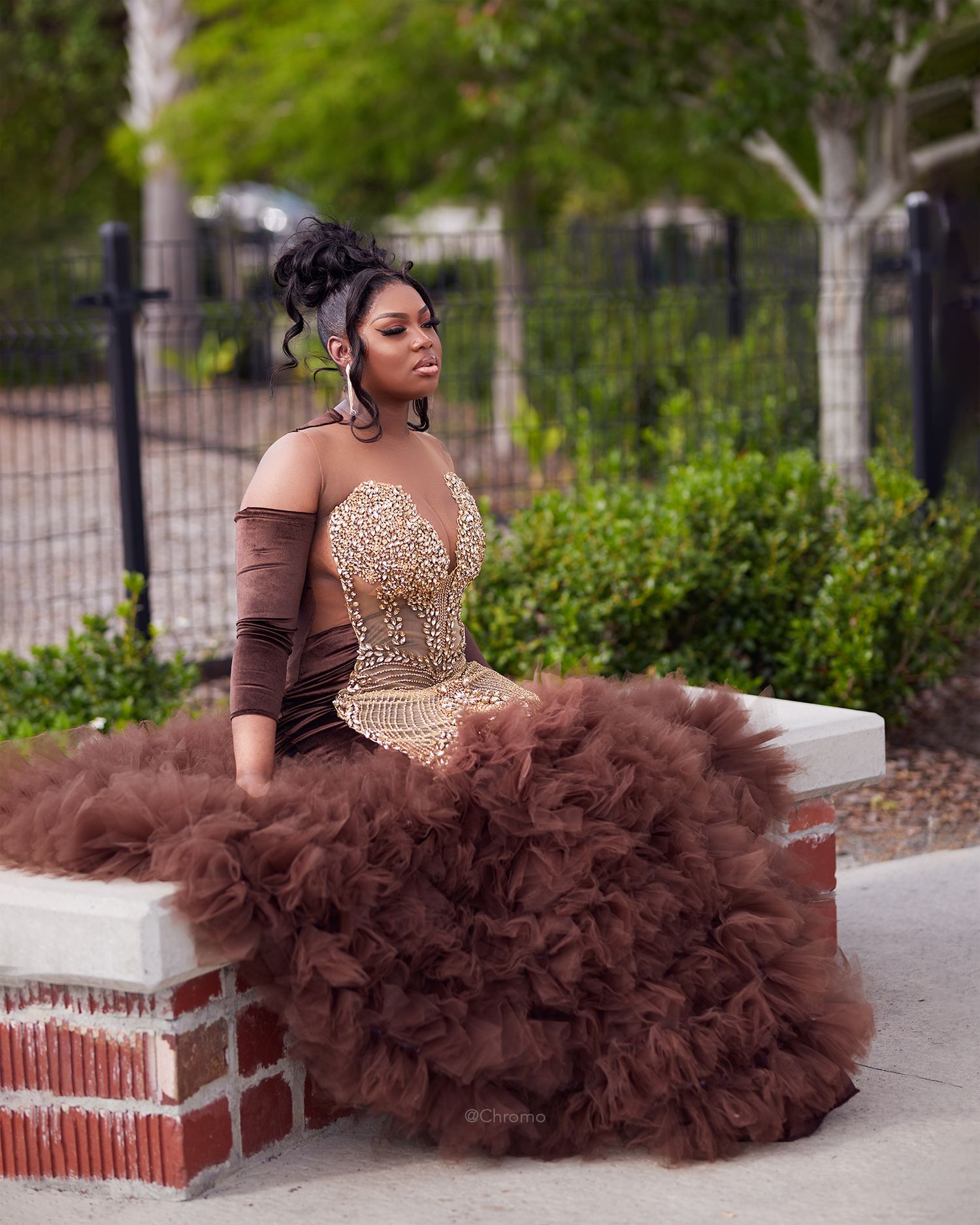 Elegant portrait of woman in brown tulle ball gown with beaded bodice seated outdoors.