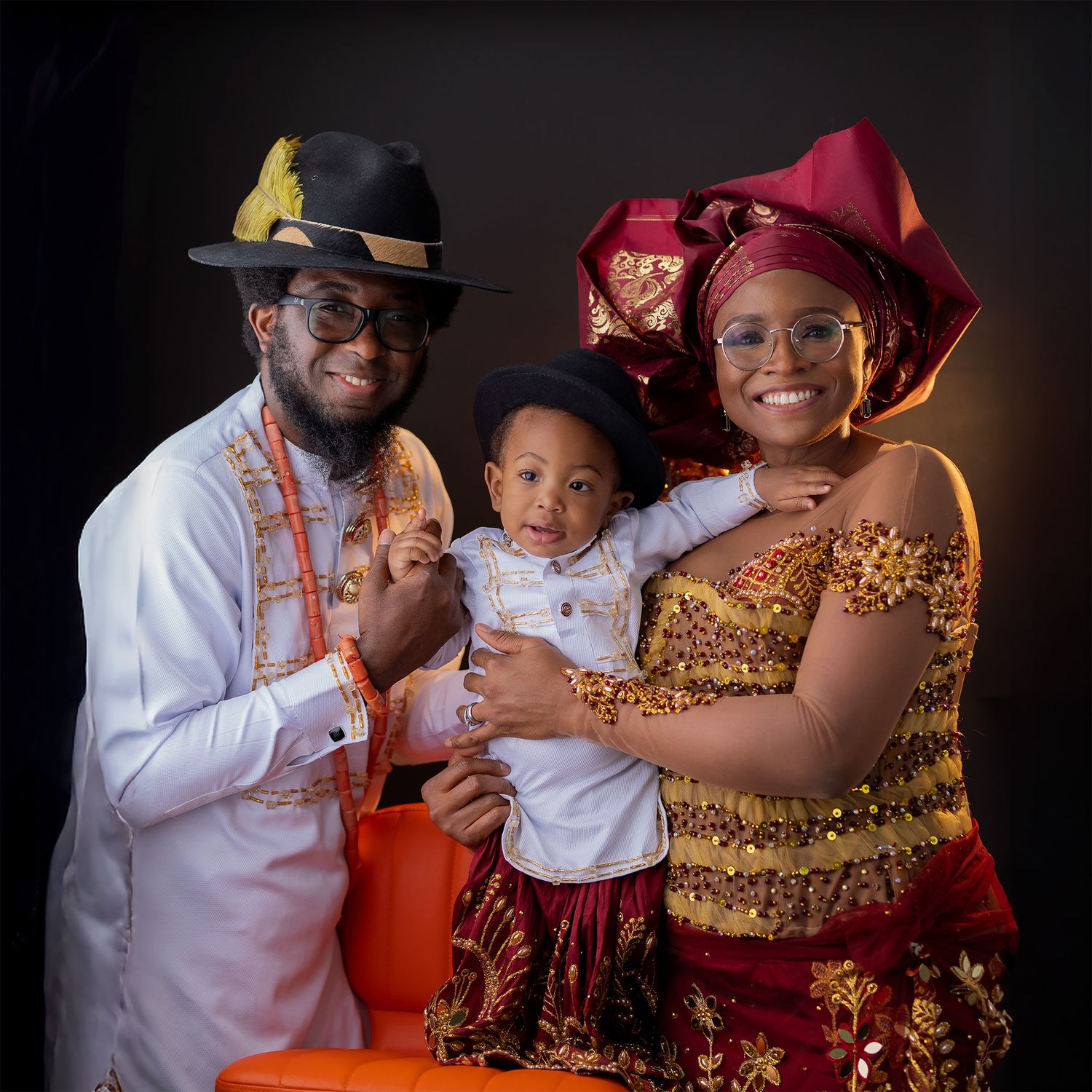 A family wearing traditional Nigerian attire poses together for a formal portrait against a dark background.