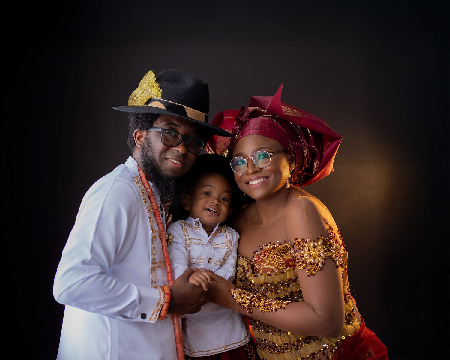 A couple in traditional African attire poses intimately against a dark background during a wedding photoshoot.