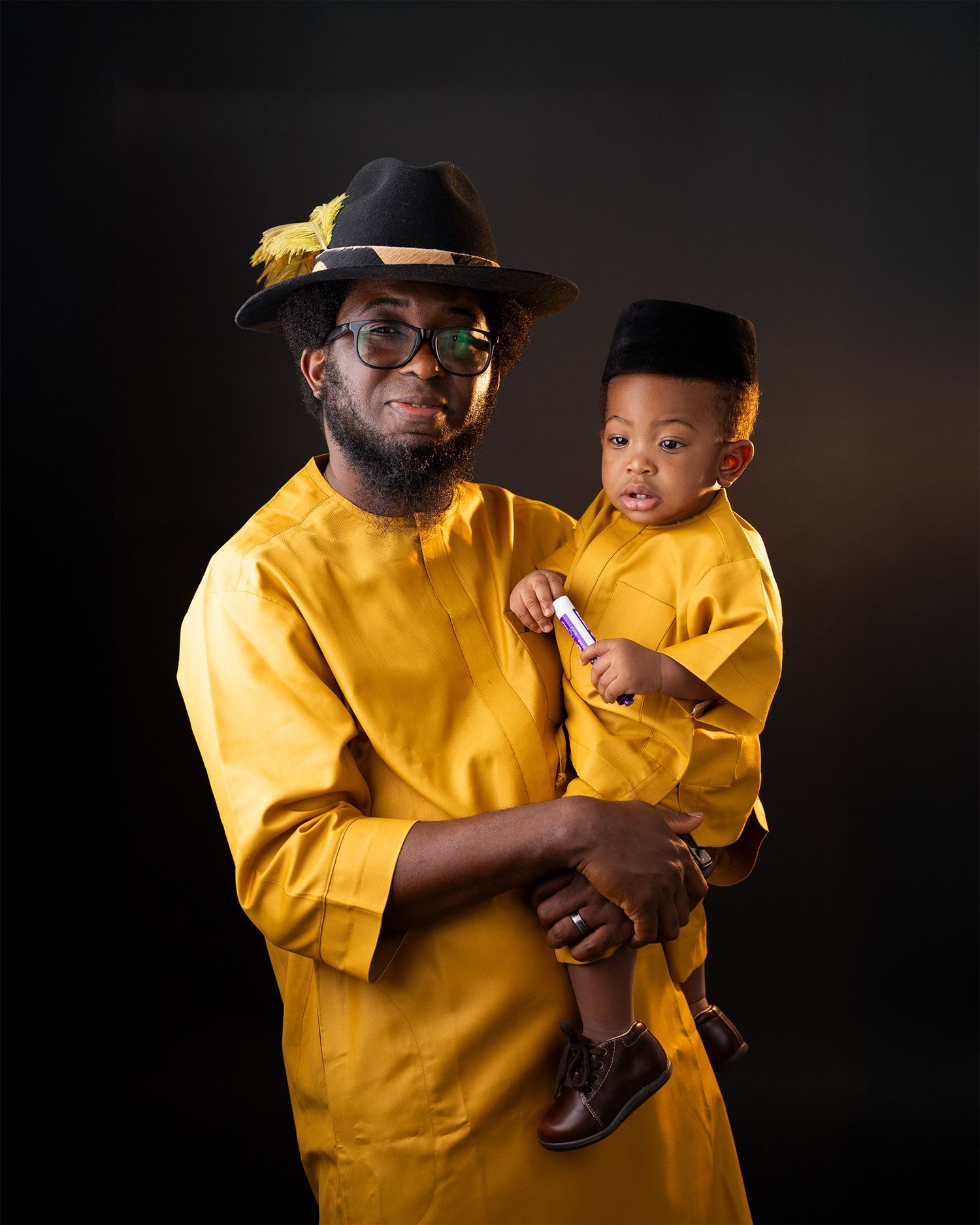 A parent and child wearing matching yellow outfits pose together against a dark background in a studio portrait.