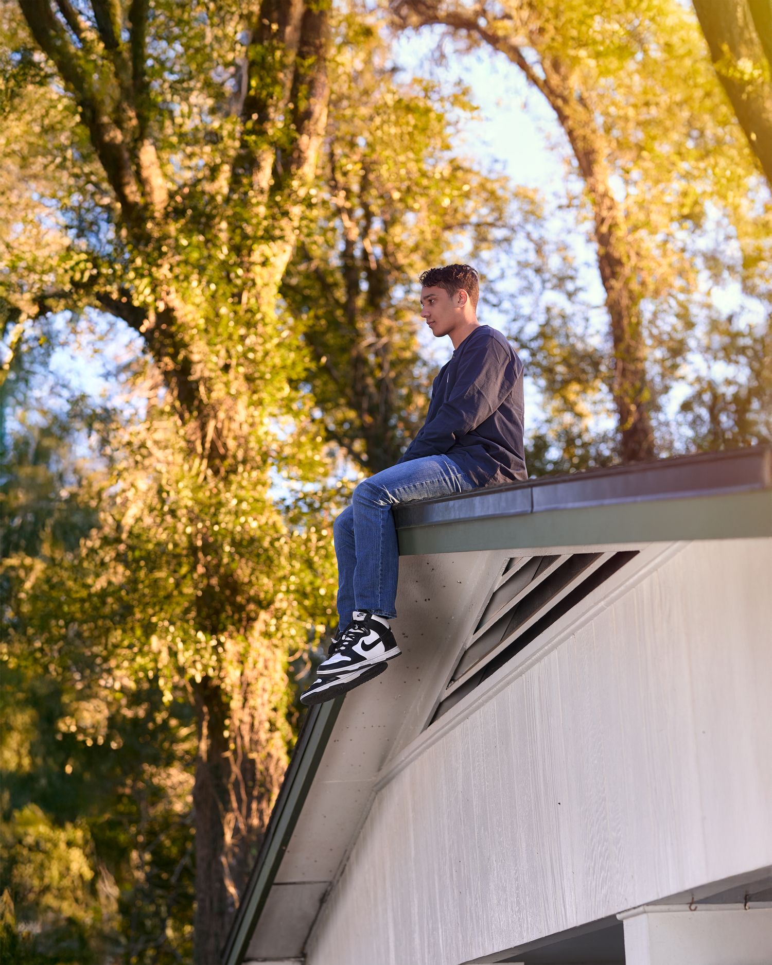 Person sitting on the edge of a white building roof surrounded by autumn trees.