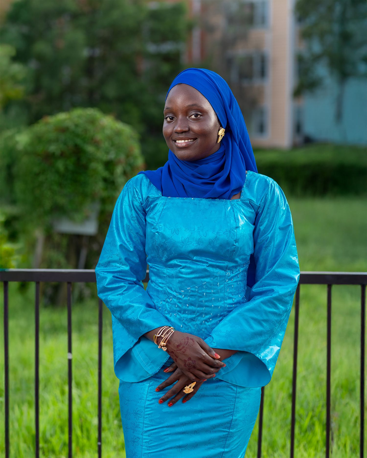 A woman in traditional dress smiles warmly while wearing a vibrant blue hijab and matching turquoise outfit.
