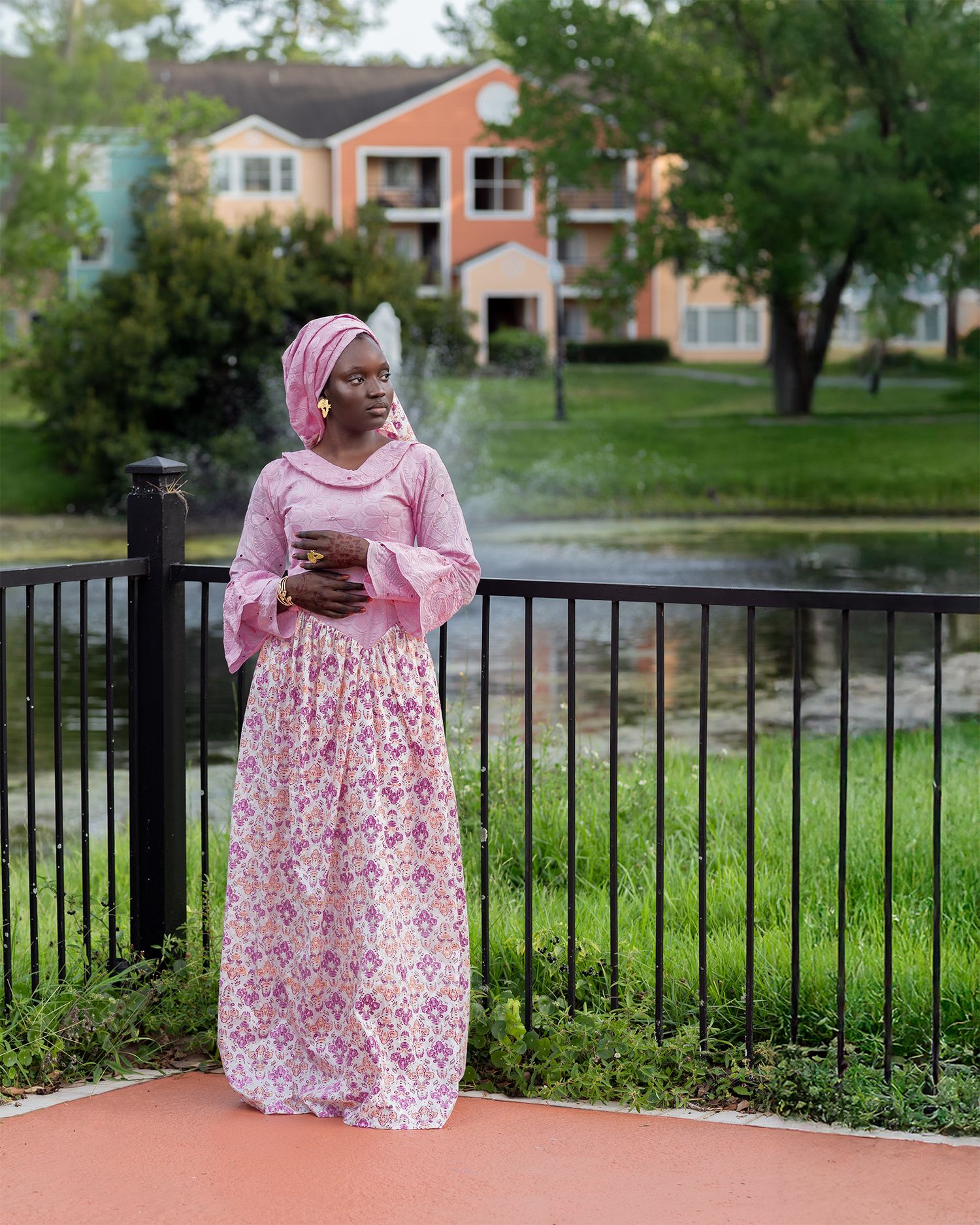 Pink floral dress against a green outdoor backdrop with metal fencing and landscaping.