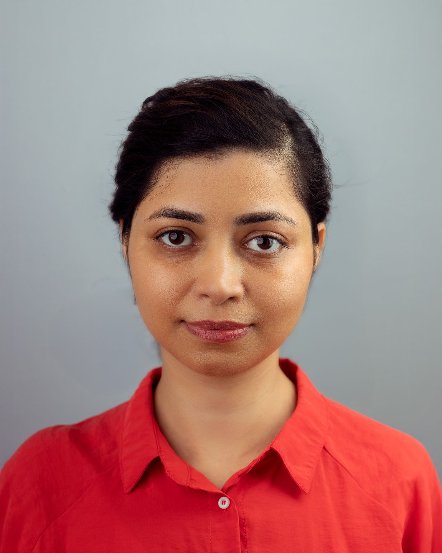 Professional headshot of a person in a red collared shirt against a gray background.
