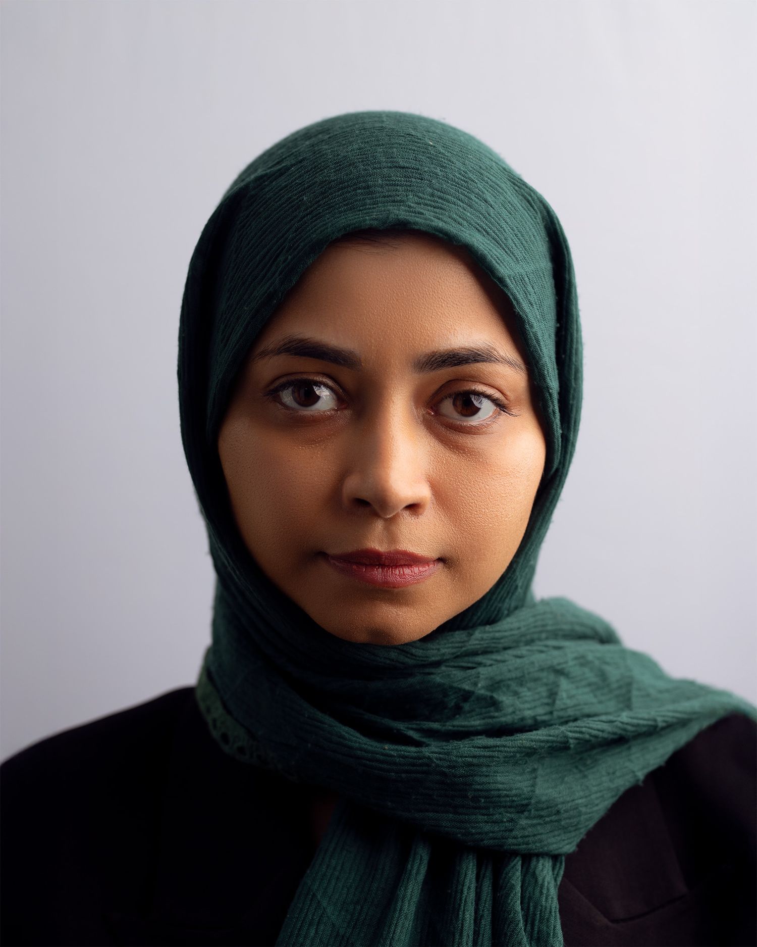 Portrait photo of someone wearing an emerald green hijab against a light gray background.