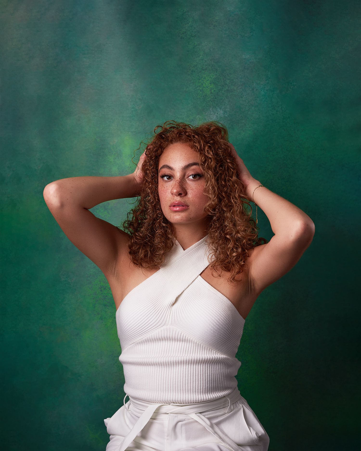Fashion portrait with green backdrop of model in white halter top with curly hair.