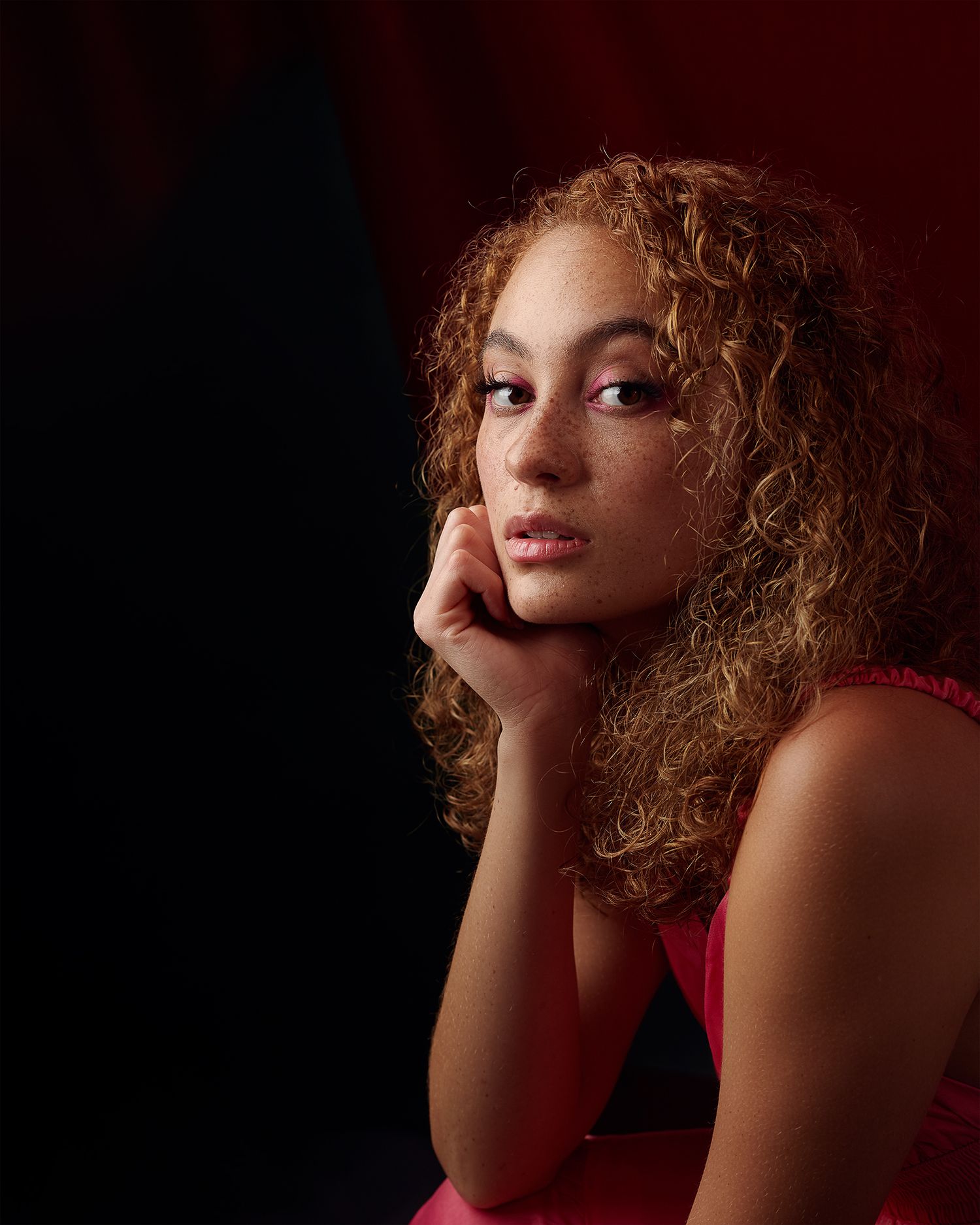 Artistic portrait with moody lighting against dark background in red attire.