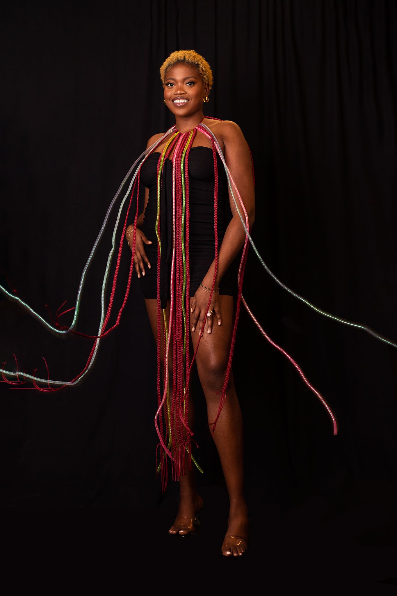 Artistic fashion portrait with dramatic red and silver string art draping against black background.