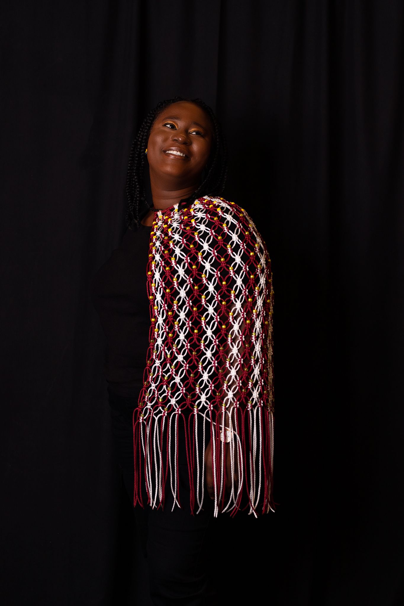 Fashion portrait against black backdrop featuring a red and white patterned fringed shawl.