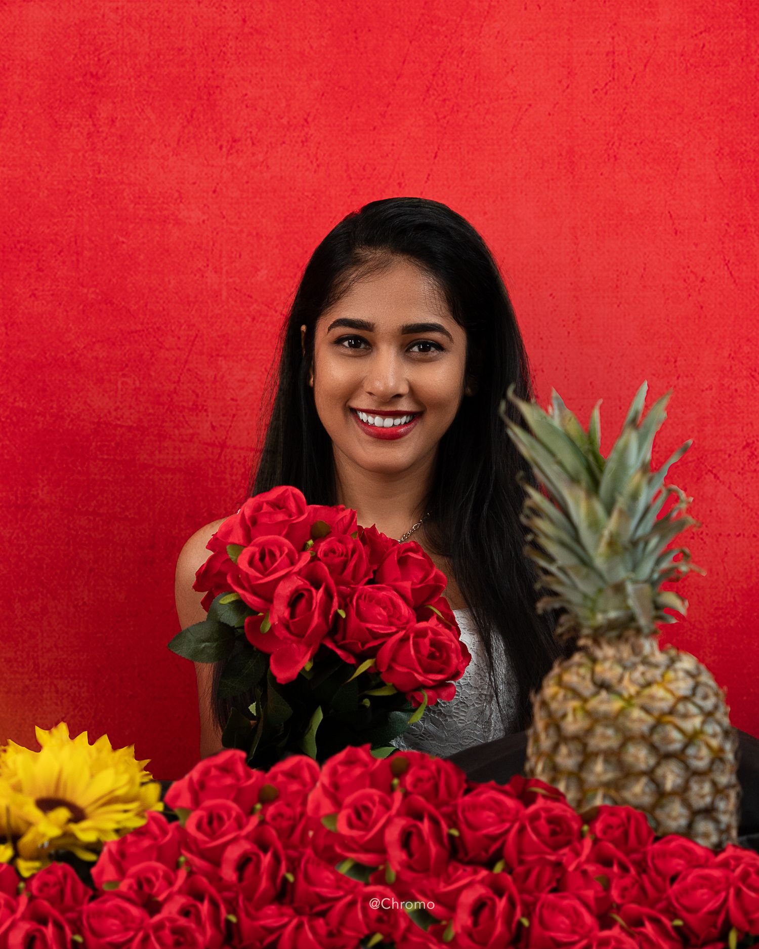 Vibrant portrait with red roses, sunflower, and pineapple against a bright red background.