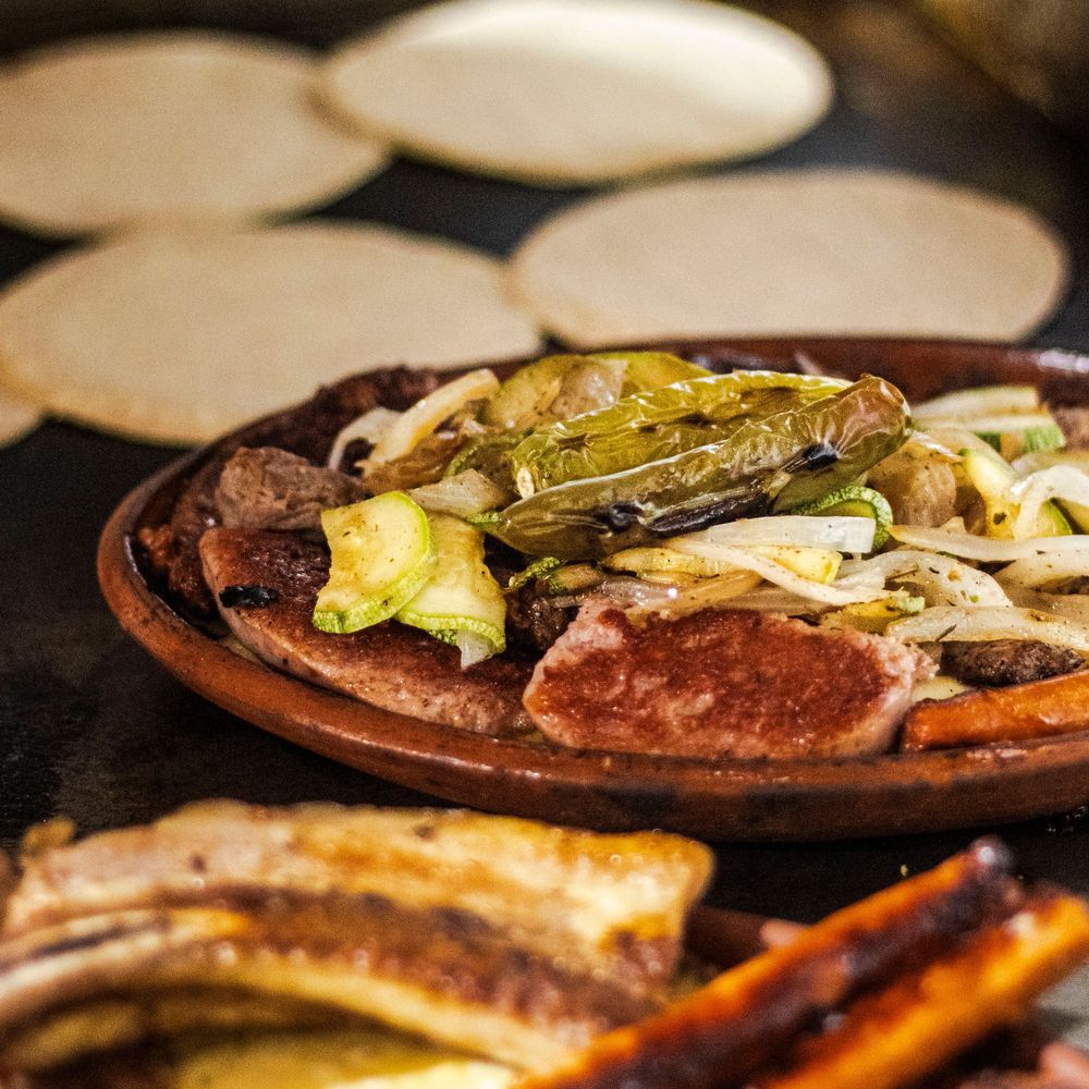 Traditional Mexican carne asada platter with grilled nopales, onions, and tortillas on clay dish.