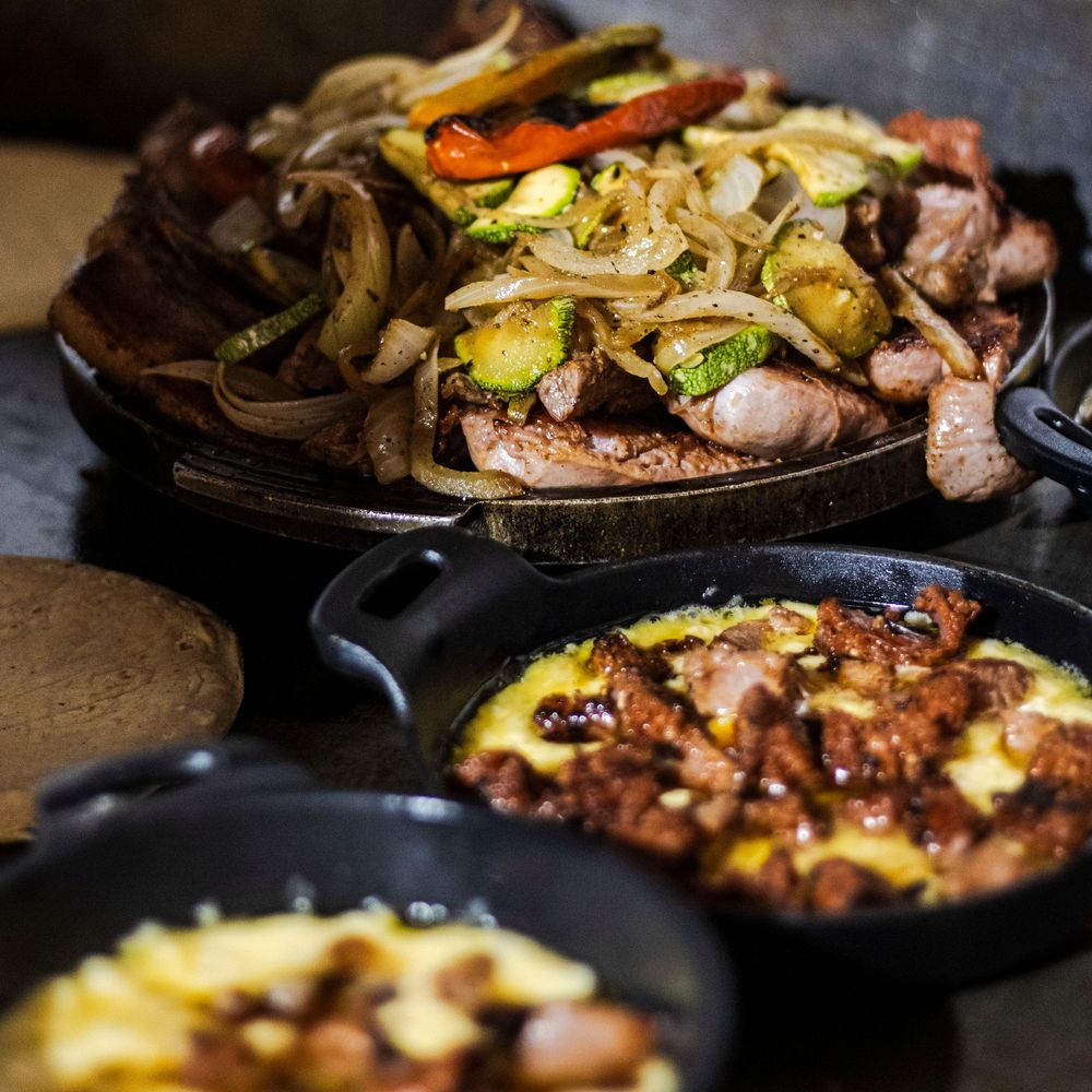 Sizzling fajitas with grilled vegetables and meat served in cast iron skillets on rustic table.