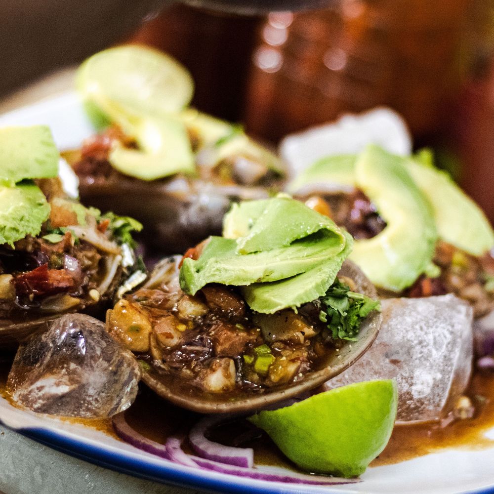 Fresh seafood cocktail topped with avocado slices, lime, and savory broth served on ice.