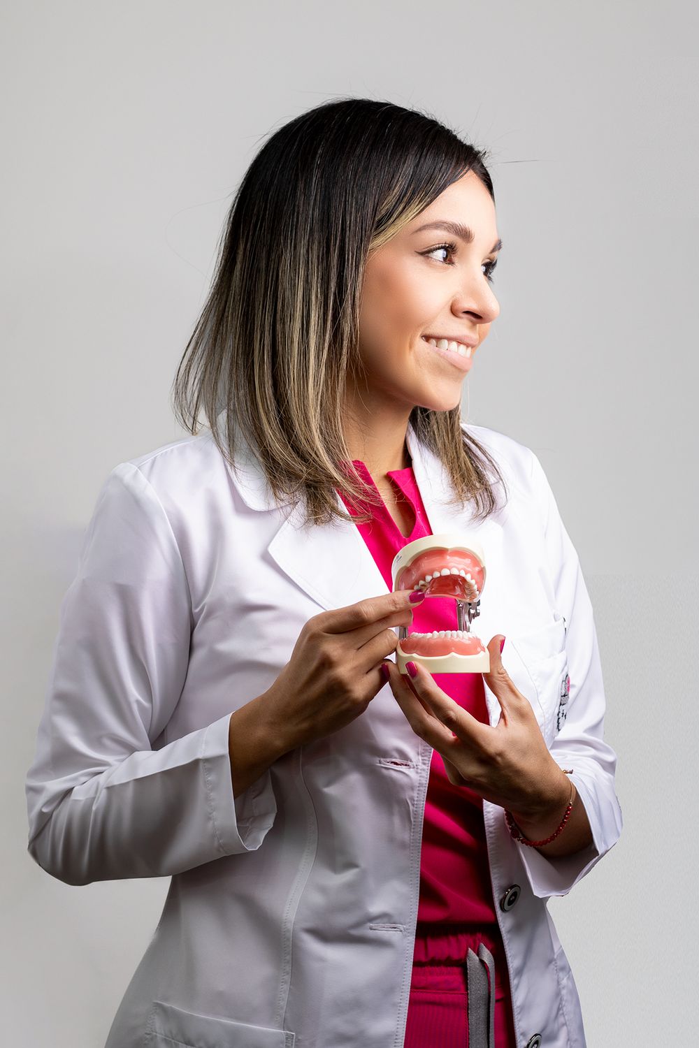 Smiling female dentist in white lab coat holding dental jaw model in studio.