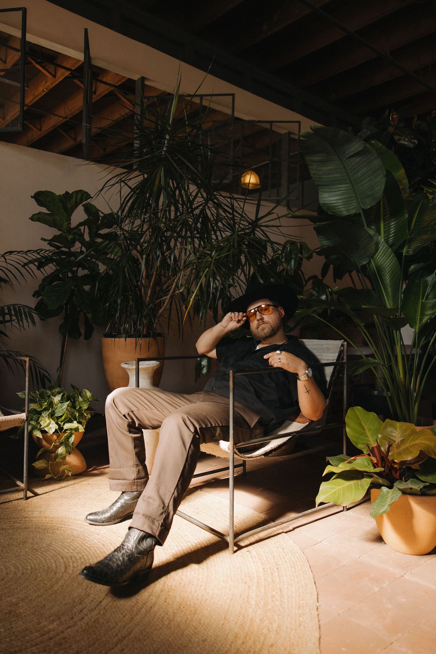 A creative portrait of a photographer relaxing in a chair surrounded by lush indoor plants at night.