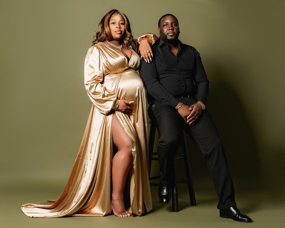 Glamorous couple poses in formal attire against olive green backdrop.