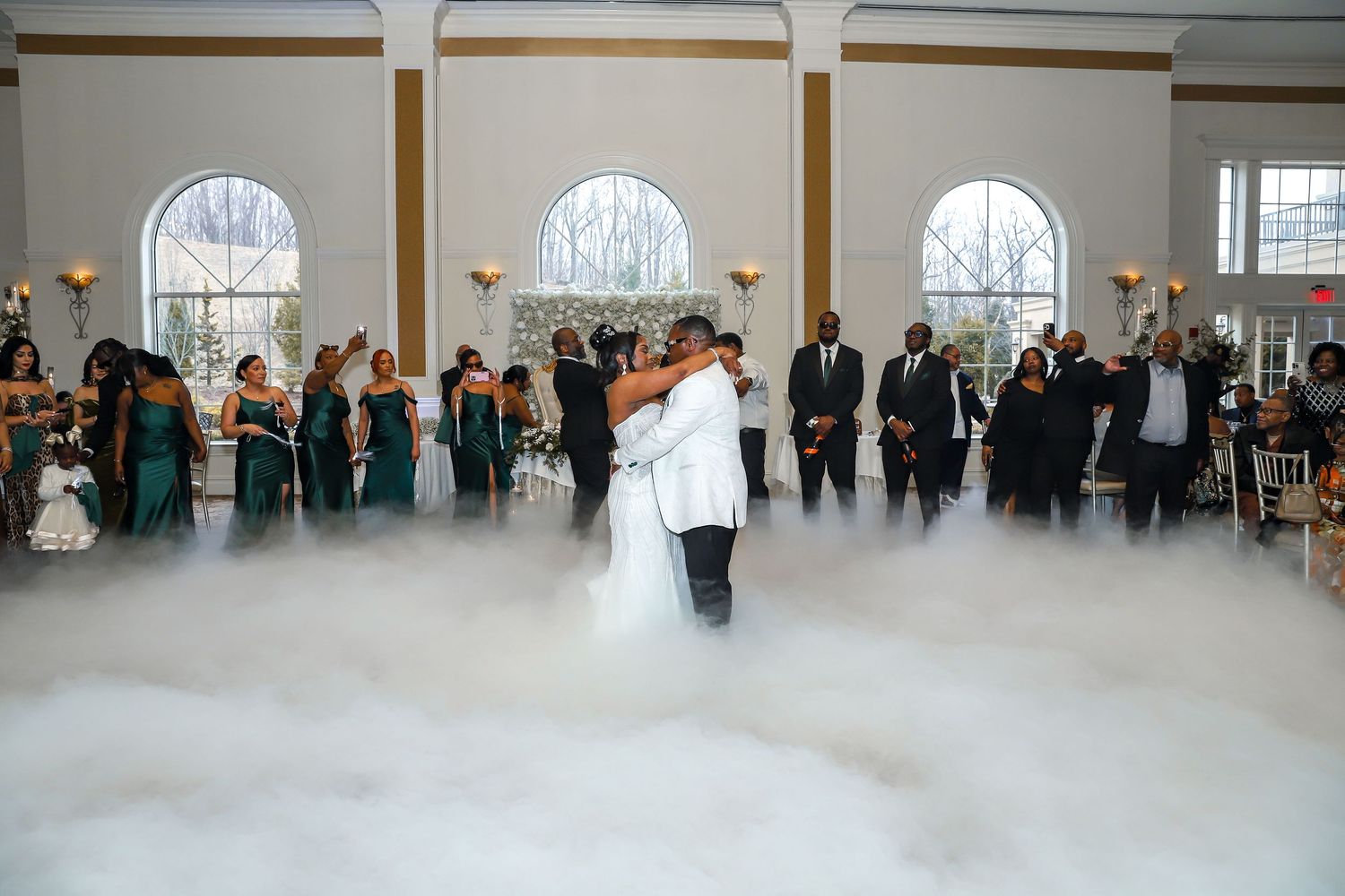 Wedding reception dancers spread across a bright indoor venue with white ceiling drapes and muted lighting.