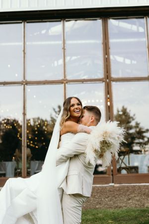 Joyful wedding moment with couple in white attire by large windows.