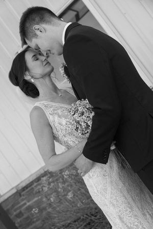 A romantic black and white wedding portrait shows a tender moment between newlyweds in elegant formal attire.